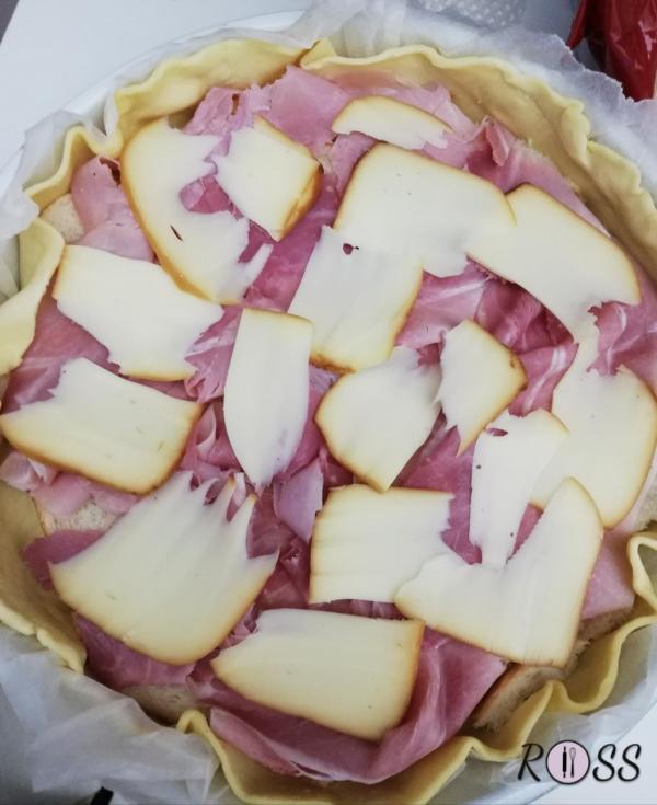 Prendete una teglia rotonda da 22 cm, rivestitela con carta forno, ponetevi sopra la pasta brisée, cospargete qualche cucchiaio di ricotta, aggiungete  il prosciutto in un unico strato e le fette di provola affumicata.