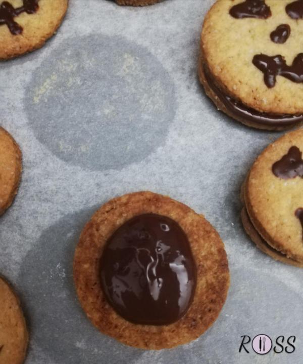 Infornate. Nel frattempo iniziate a sciogliere a bagnomaria il cioccolato fondente e procuratevi una siringa(privata di ago) per decorare i biscotti. Appena questi saranno cotti, estraeteli dal forno, lasciateli raffreddare leggermente ed iniziate a decorare metà dei biscotti con il cioccolato fondente dentro la siringa